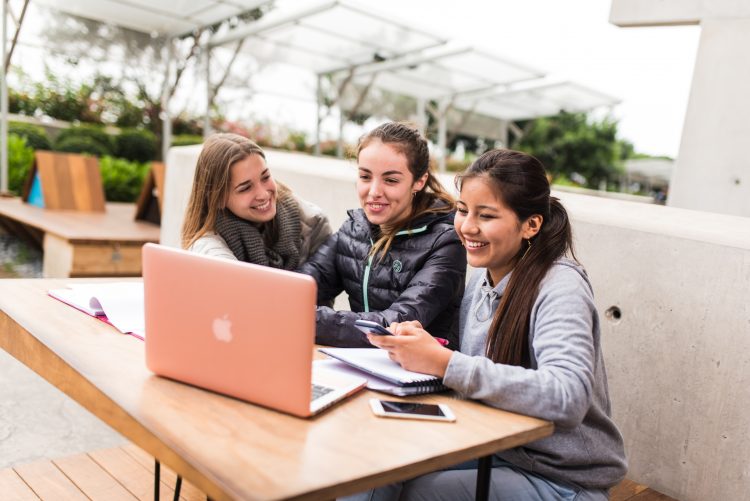 Tres estudiantes revisan una MacBook en el campus de UTEC mientras conversan sobre becas universitaria