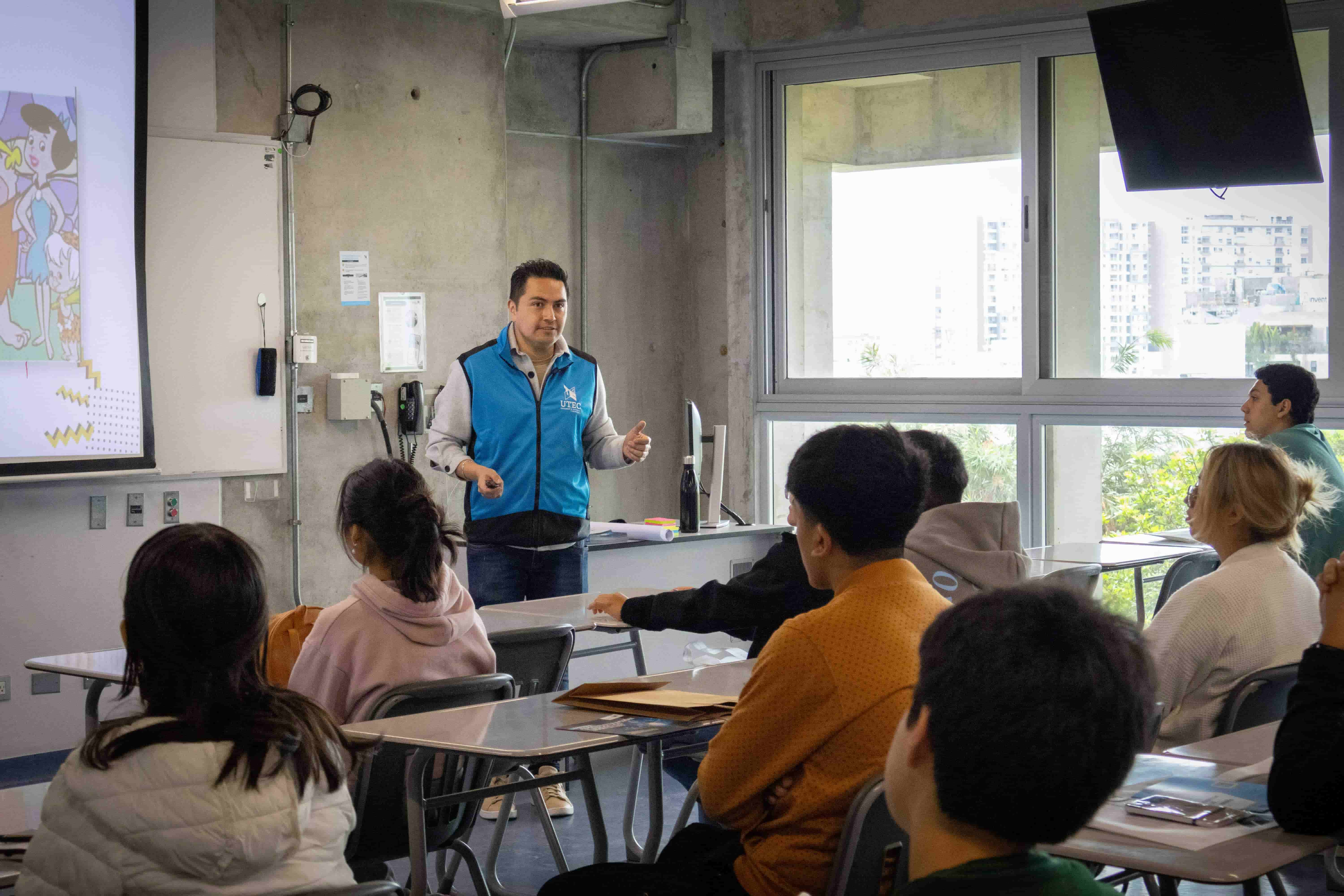  Un orador con chaleco azul da una charla informativa en un aula de clase a un grupo de jóvenes interesados en becas para universitarios