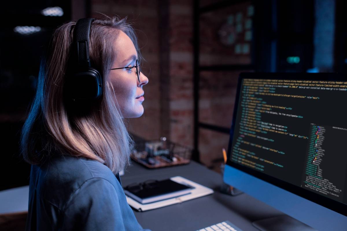 Una profesional de ciberseguridad con auriculares y gafas analiza líneas de código en un monitor durante una auditoría de seguridad nocturna